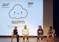 four people sitting on chairs in front of a large screen with the words happy written on it