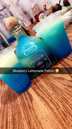 two bottles of blueberry lemonade patron on a wooden table with glasses in the background