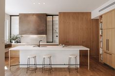 a kitchen with wooden cabinets and white counter tops, along with bar stools that match the hardwood flooring