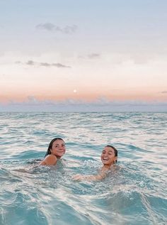 two women swimming in the ocean at sunset