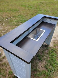 an outdoor table with a sink in the middle of it on some grass and dirt