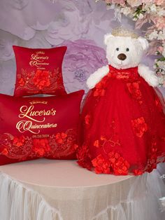 a white teddy bear wearing a red dress sitting next to two pillows with roses on them