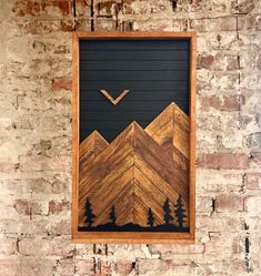 a wooden frame hanging on a brick wall with mountains and trees painted on the side