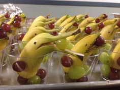 bananas and grapes are arranged in plastic cups on a metal tray with silver foil wrappers