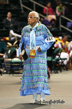 an older man wearing a blue dress and holding a cup in his hand while standing on a basketball court