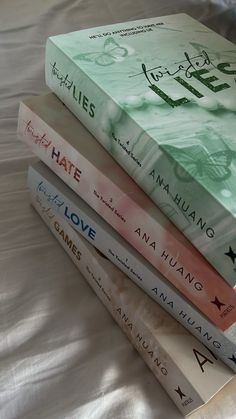 four books stacked on top of each other in front of a white bed sheet with the covers pulled down