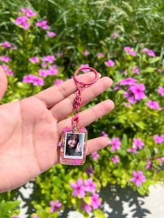 a hand holding a pink keychain with a photo hanging from it's end