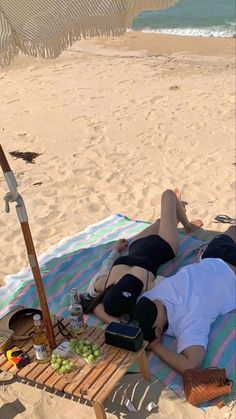 a woman laying on top of a beach next to an umbrella and picnic table filled with food