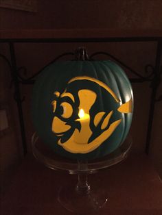 a green and yellow pumpkin with a fish on it's face sitting on a glass stand