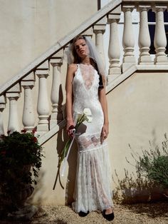 a woman in a wedding dress standing next to a stair case and holding a bouquet