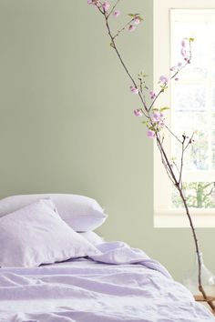 a bed with purple sheets and pillows next to a vase with pink flowers on it