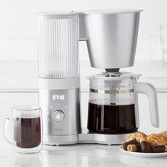 a coffee maker sitting on top of a counter next to a plate of cookies and chocolates