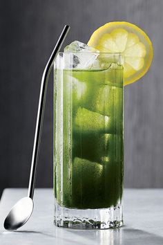 a tall glass filled with green liquid and lemon wedges next to a silver spoon