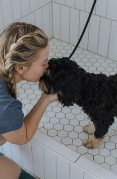 The owner of this mid-century modern remodel using their modern dog wash and giving a kiss to their little puppy. Featured; Delta hand-held shower, white hexagon floor tile, and white subway tile.