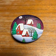 a painted rock on a wooden table with trees and houses in the snow at night