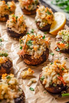 small stuffed mushrooms with various toppings on a sheet of wax paper next to lemon wedges and parsley