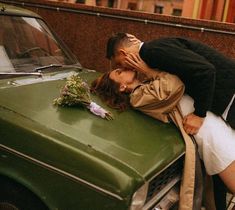 a man and woman kissing on the hood of a green car