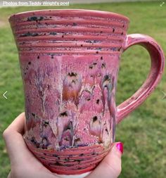 a hand holding a pink coffee cup with birds on it in front of some grass