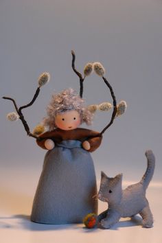 a doll and cat sitting next to each other in front of a gray background with white flowers