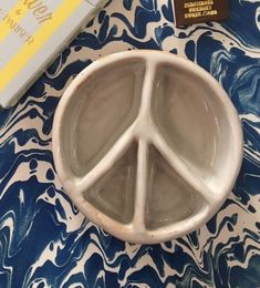 a peace sign bowl sitting on top of a blue and white table cloth next to a book