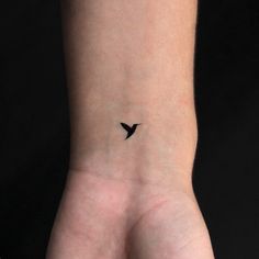 a small black bird tattoo on the left inner wrist, with an arrow in it's center