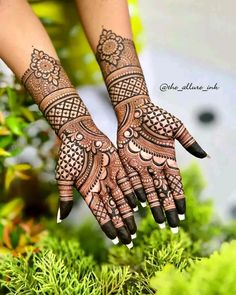 two hands with henna tattoos on them and green plants in the foregrounds