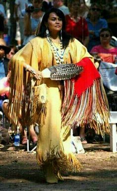 a native american woman dressed in yellow and holding a red object while standing next to a crowd