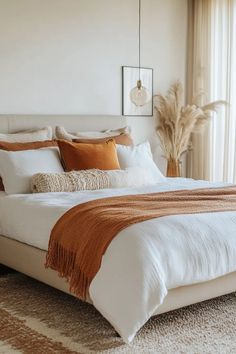 a bed with white sheets and orange pillows in a bedroom next to a large window