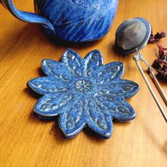 a blue ceramic flower sitting on top of a wooden table next to a tea strainer