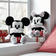 two stuffed mickey mouses sitting on top of a window sill next to a christmas present