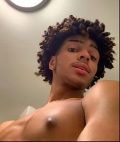 a young man with curly hair and no shirt is looking at the camera while standing in front of a mirror