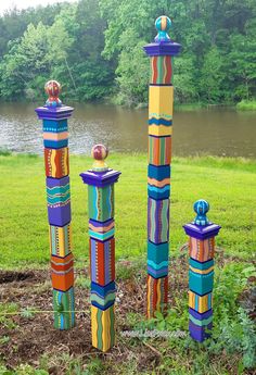 three colorfully painted poles in the grass near water