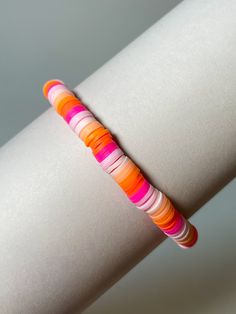 an orange, pink and white striped bracelet on top of a roll of paper in front of a gray background