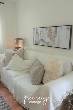 a living room with white couches, pillows and a painting hanging on the wall