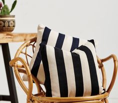 two black and white striped pillows sitting on a wicker chair next to a table