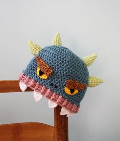 a crocheted hat with horns and eyes on top of a wooden chair against a white wall