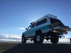 a white and green truck parked on top of a dirt field next to a blue sky