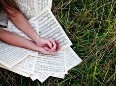 a woman laying on top of sheet music in the grass with her hands resting on it