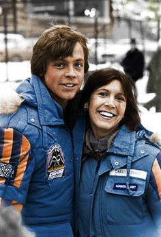 a man and woman in blue jackets posing for a photo outside on a snowy day