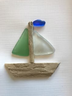 a sailboat made out of sea glass on a piece of driftwood with two blue and one green