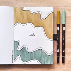 an open notebook with the word july written on it next to two markers and a pencil