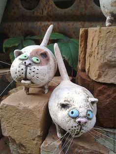 two clay cats sitting on top of rocks with one cat's head sticking out