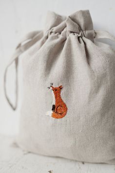 a drawstring bag with a fox embroidered on the front and back side, sitting on a white surface