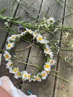 daisies laid out in the shape of a heart on a picnic table with someone's feet