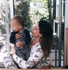 a woman holding a baby in her arms while sitting at a table with a glass door