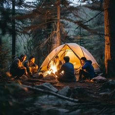 four people sitting around a campfire in the woods at night with their tent open