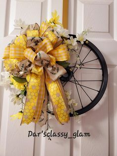 a yellow and white wreath hanging on a door with a bicycle wheel in the background