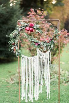 a white and gold wedding arch decorated with flowers, greenery and macrami