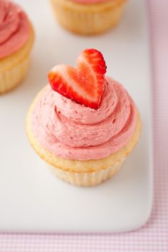 three cupcakes with pink frosting and a strawberry on top