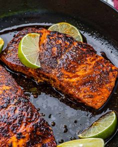 two salmon fillets in a skillet with lime wedges